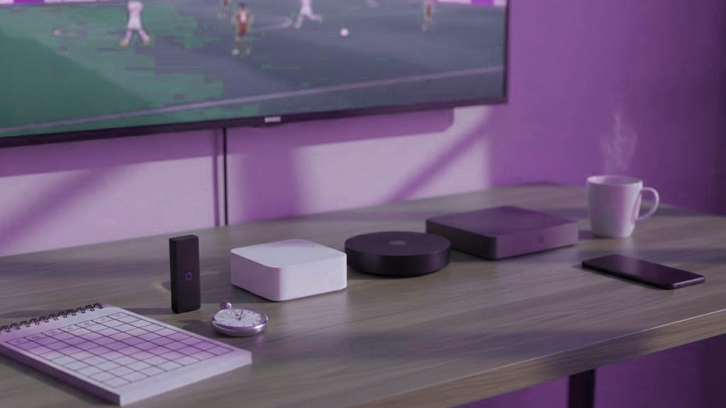 Five streaming devices, a notebook scoring grid and a stopwatch in front of a TV showing a football match