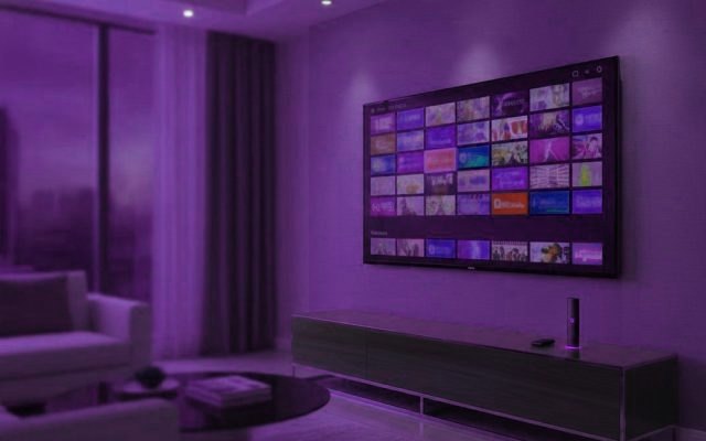 A living-room TV showing an IPTV channel guide with a streaming stick on the console